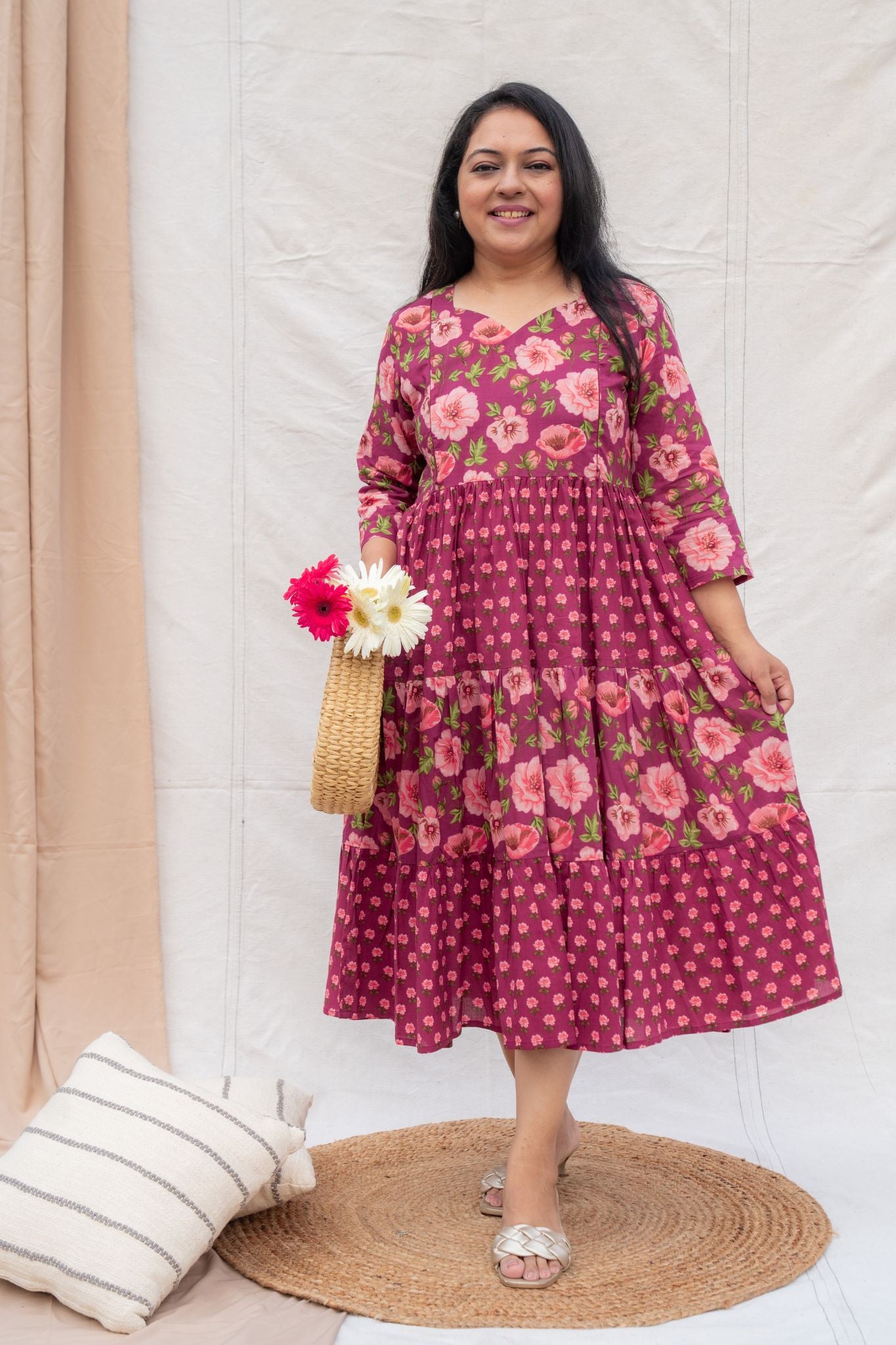 Woman wearing a pink floral dress holding flowers indoors.