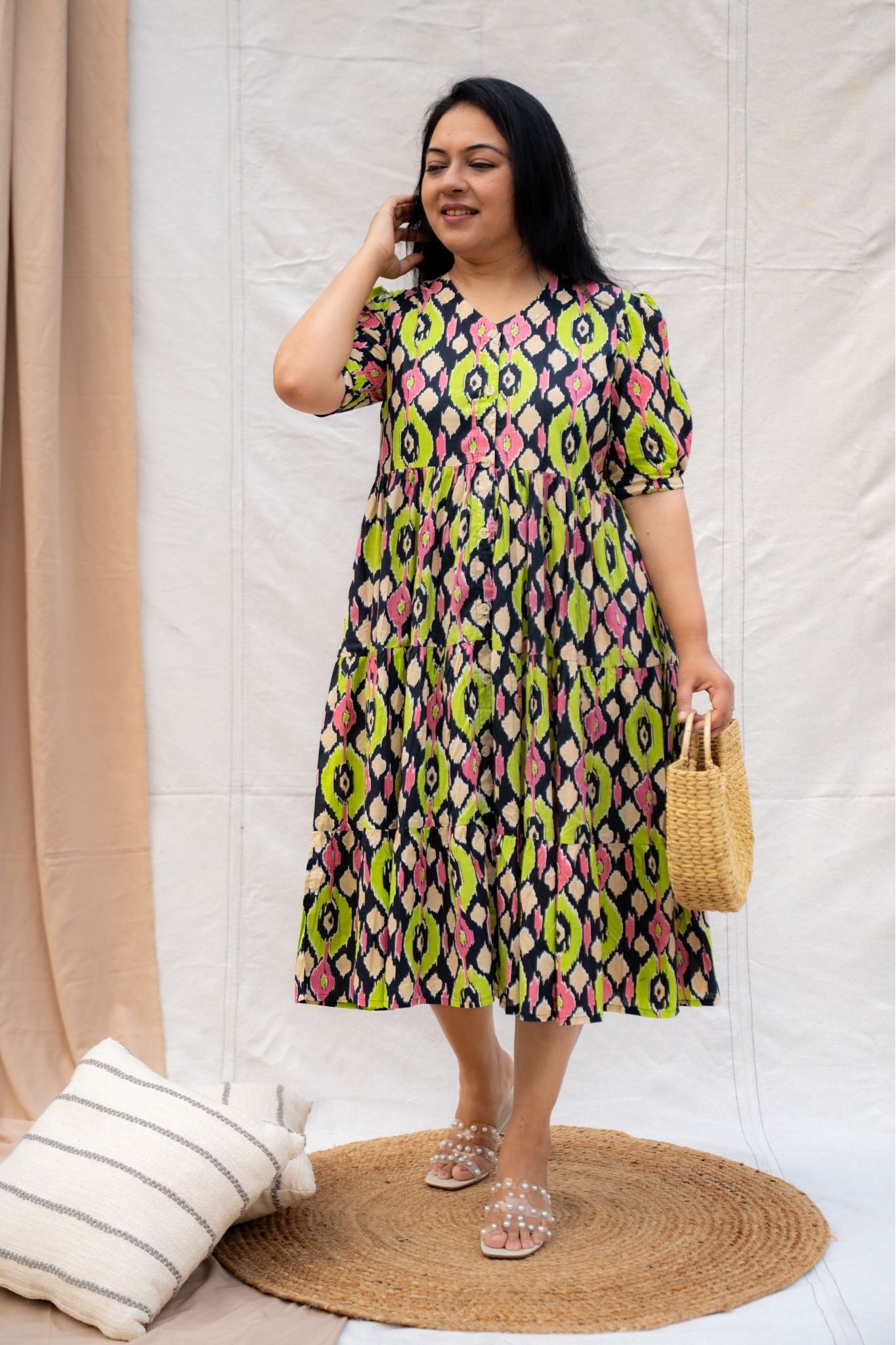 Woman wearing a colorful patterned dress standing against a white curtain.