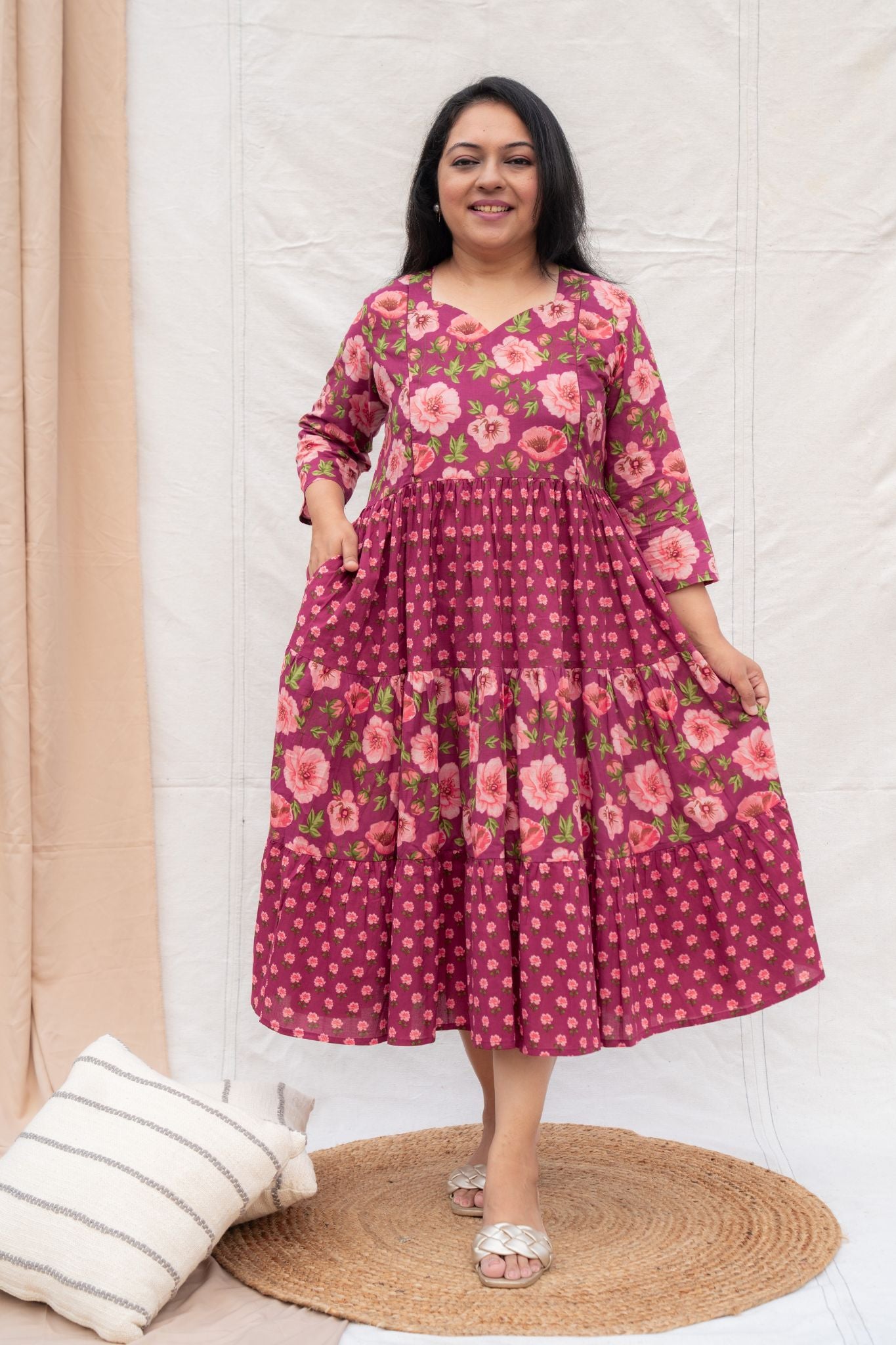 Woman wearing a pink floral dress standing against a white wall.