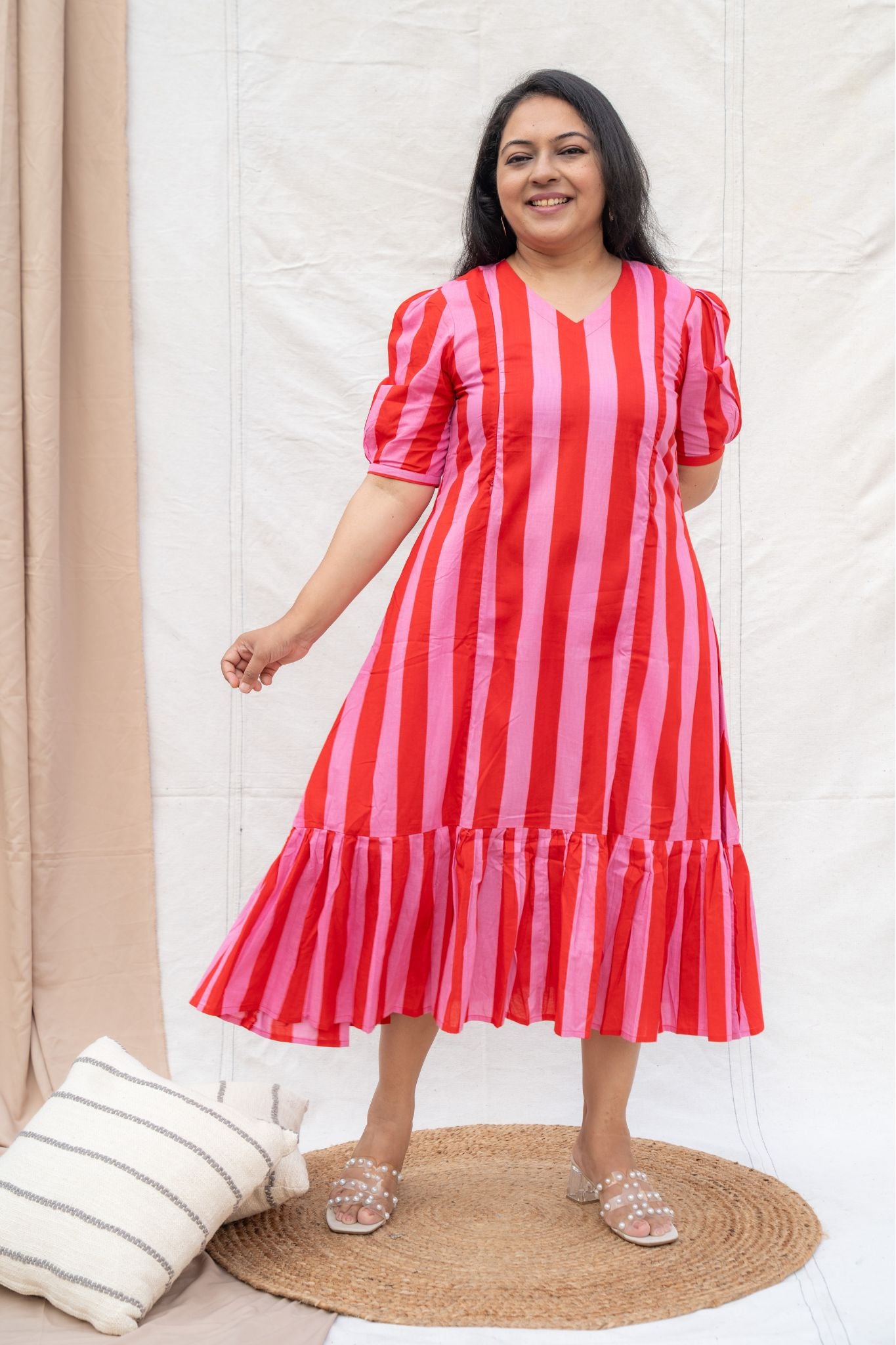 Woman wearing a red and pink striped dress standing on a beige rug with a white wall background.