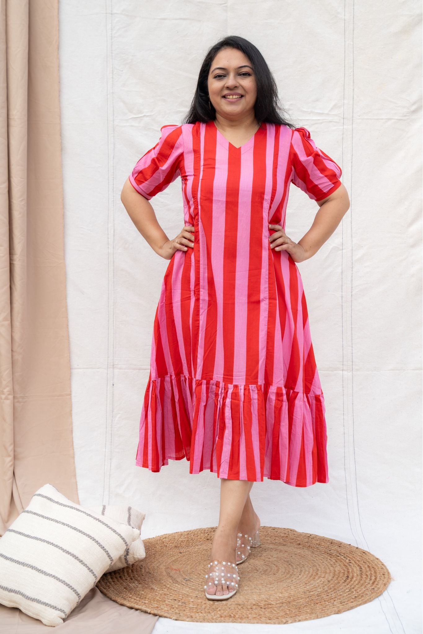 Woman wearing a red and pink striped dress standing against a white curtain.