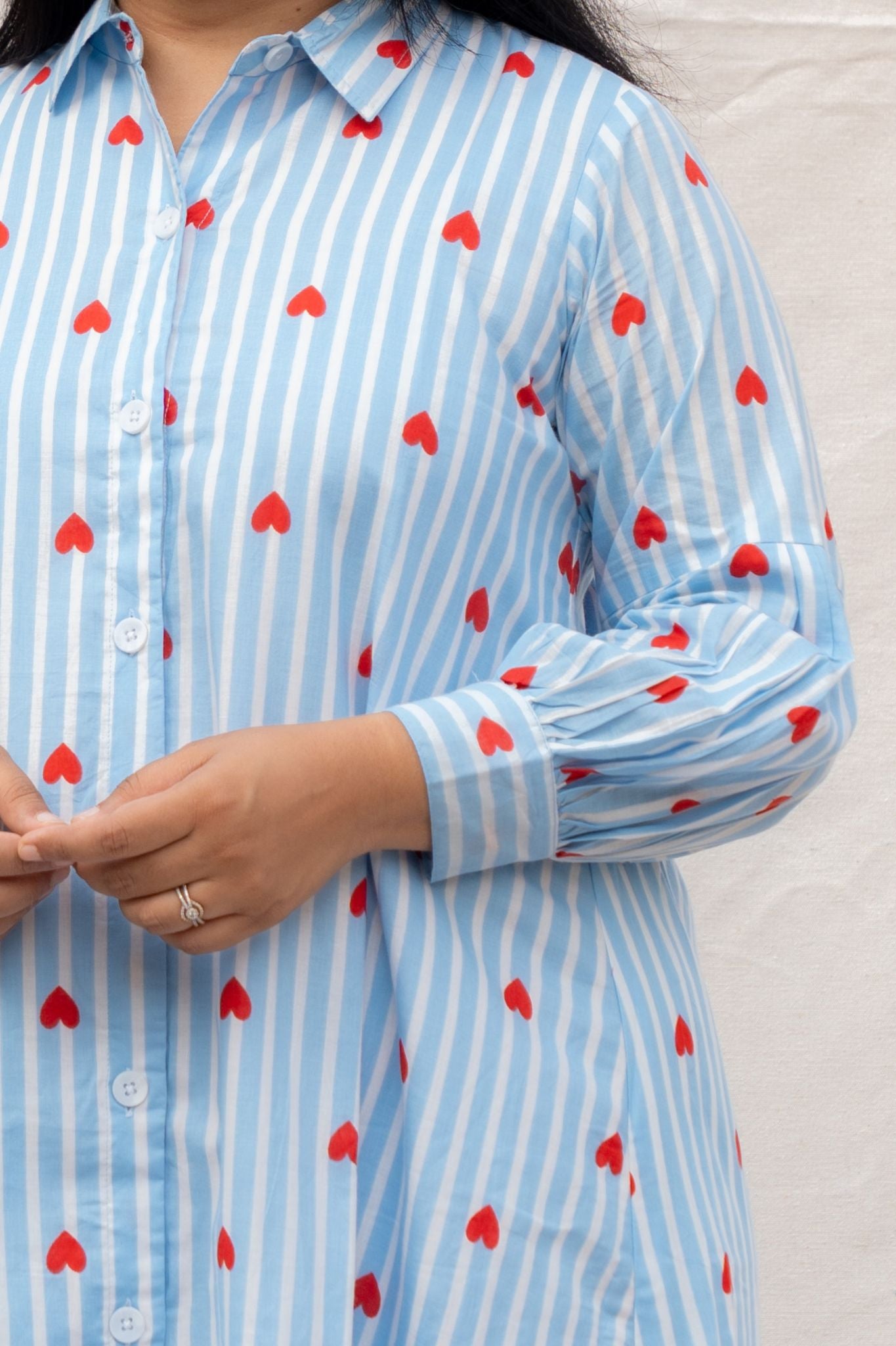 Close-up of a person wearing a blue and white striped shirt with red heart patterns.